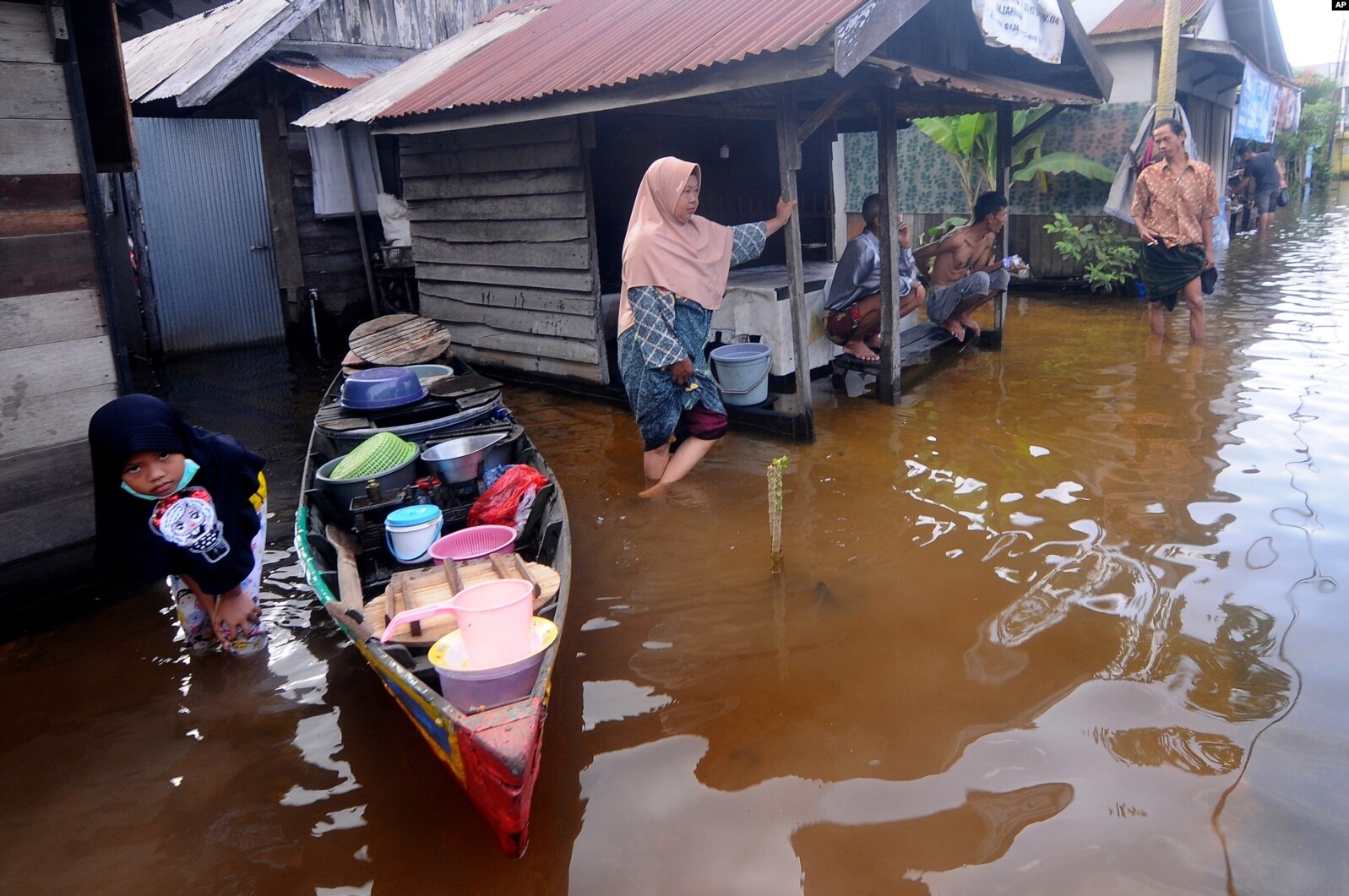Orang-orang berbicara di luar rumah mereka di lingkungan yang terkena banjir di Banjarmasin, Kalimantan Selatan. (Foto: AP)