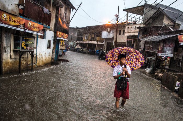 Cynthia Boll/National Geographic Indonesia Seorang pelajar melintasi jalan yang terendam banjir di pesisir utara Jakarta.